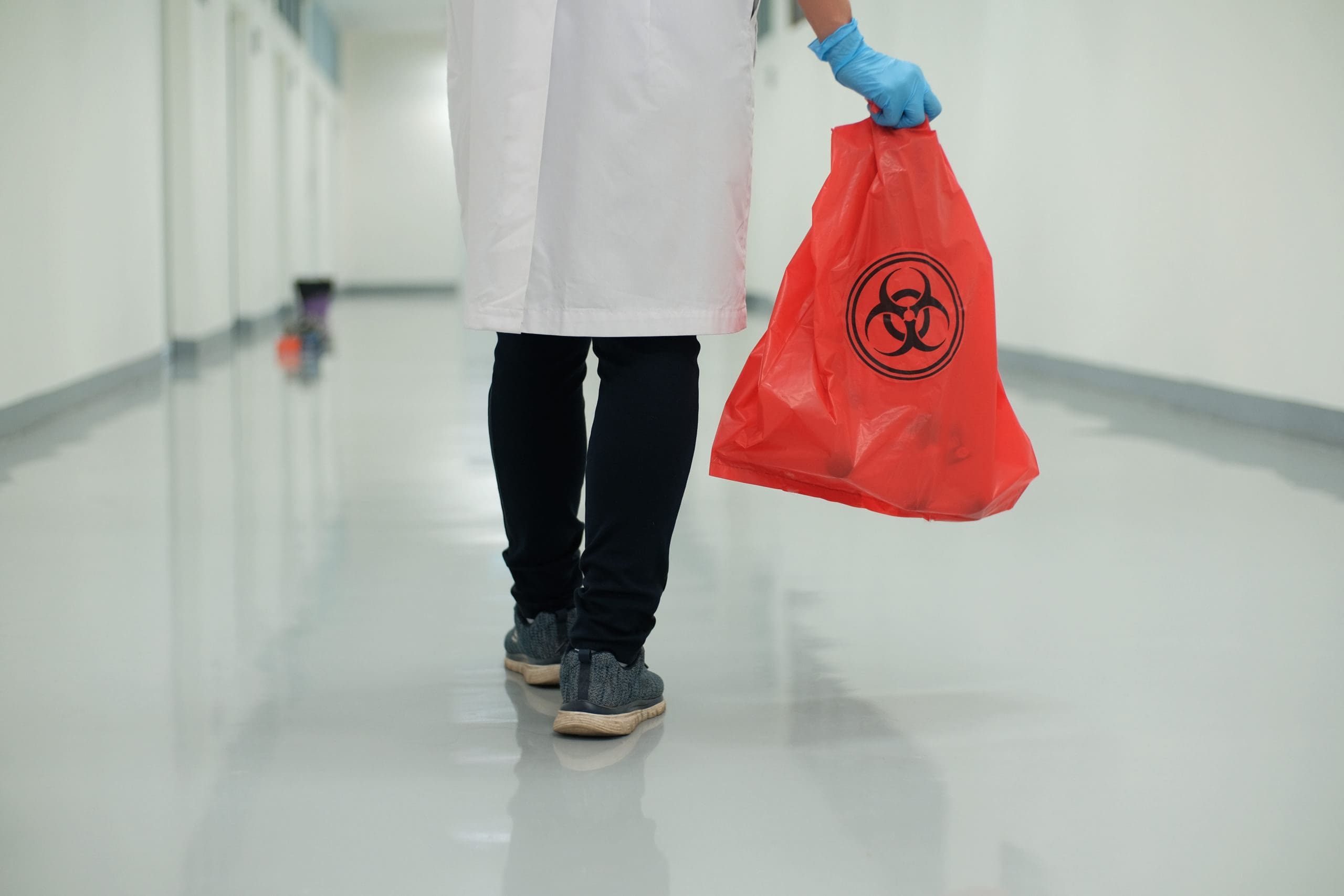 coronavirus covid-19 a medical waste management personnel carries a trash bag bearing a hazardous material symbol