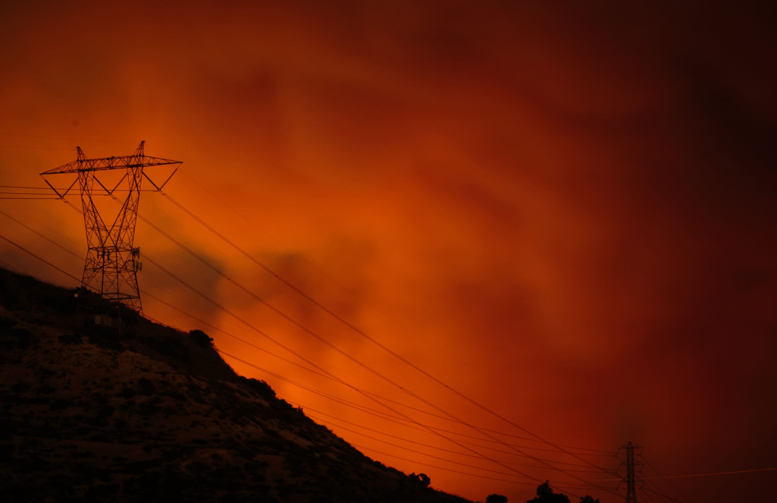California wildfires create a red sky with a utility tower showing the need for reinforced cabling