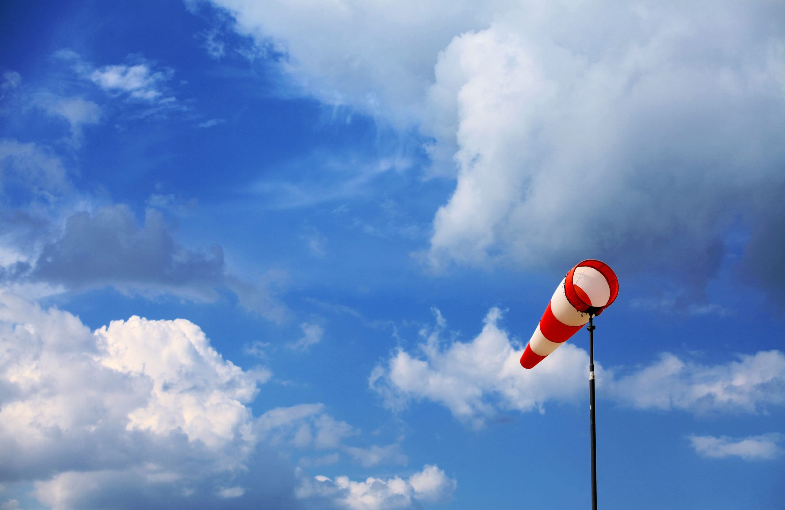 A red wind vane against a blue cloudy sky helps predict weather patterns