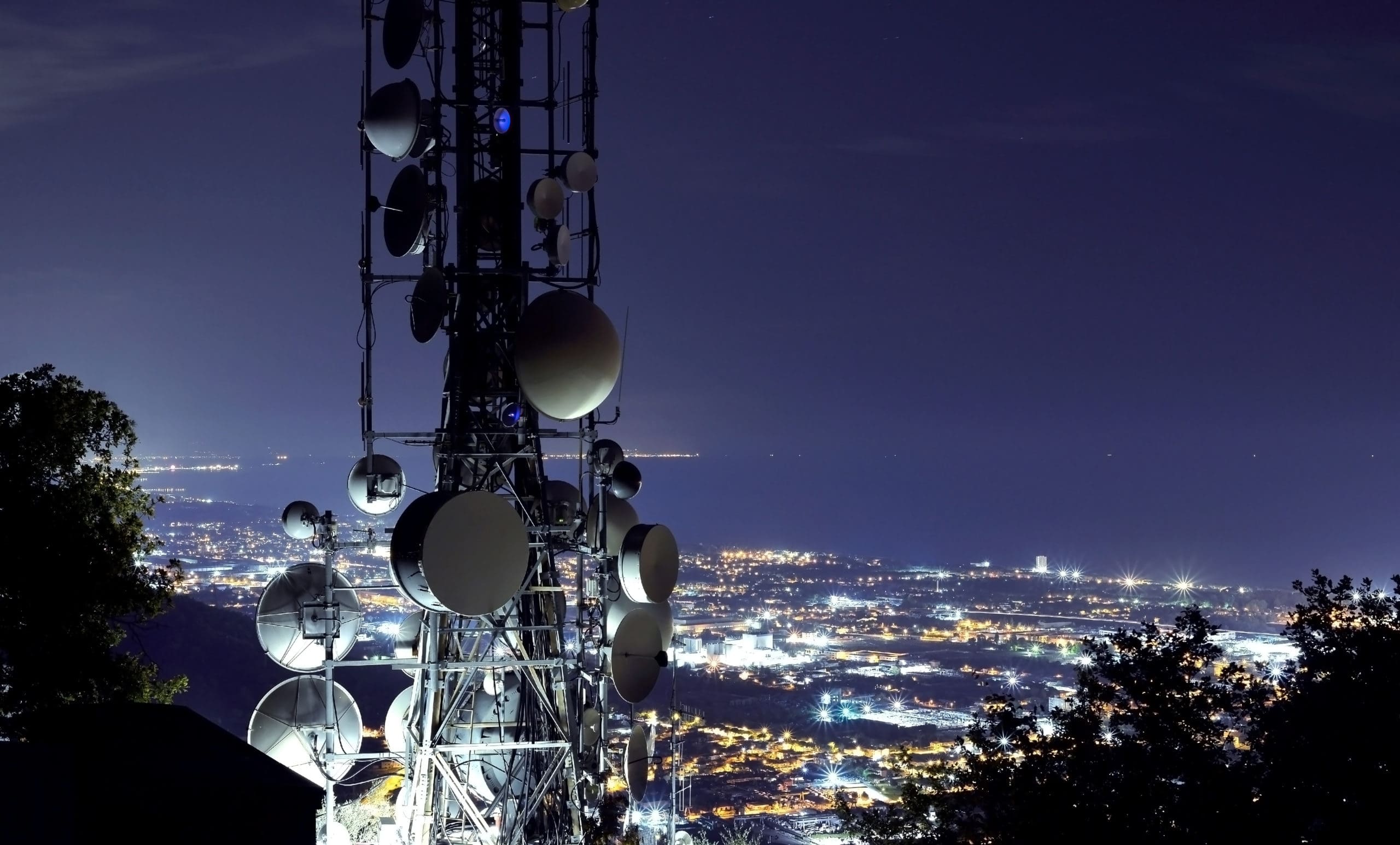 Telecommunications tower, providing access to mobile networks,, antenna and satellite dish and city at night as background