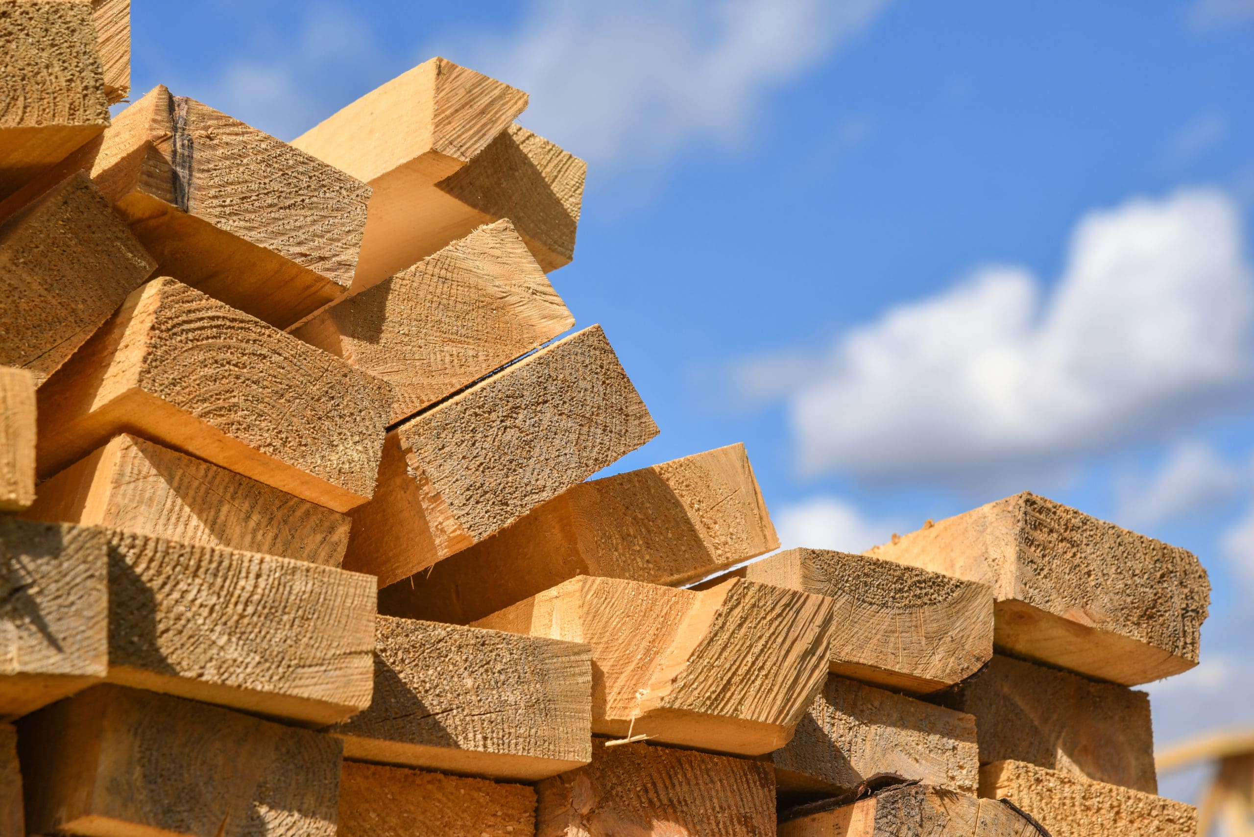 wood stacked on itself with blue sky in the background, a reference to lumber prices