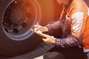 Driver worker handling clipboard check list and checking tire truck as part of routine dump truck maintenance