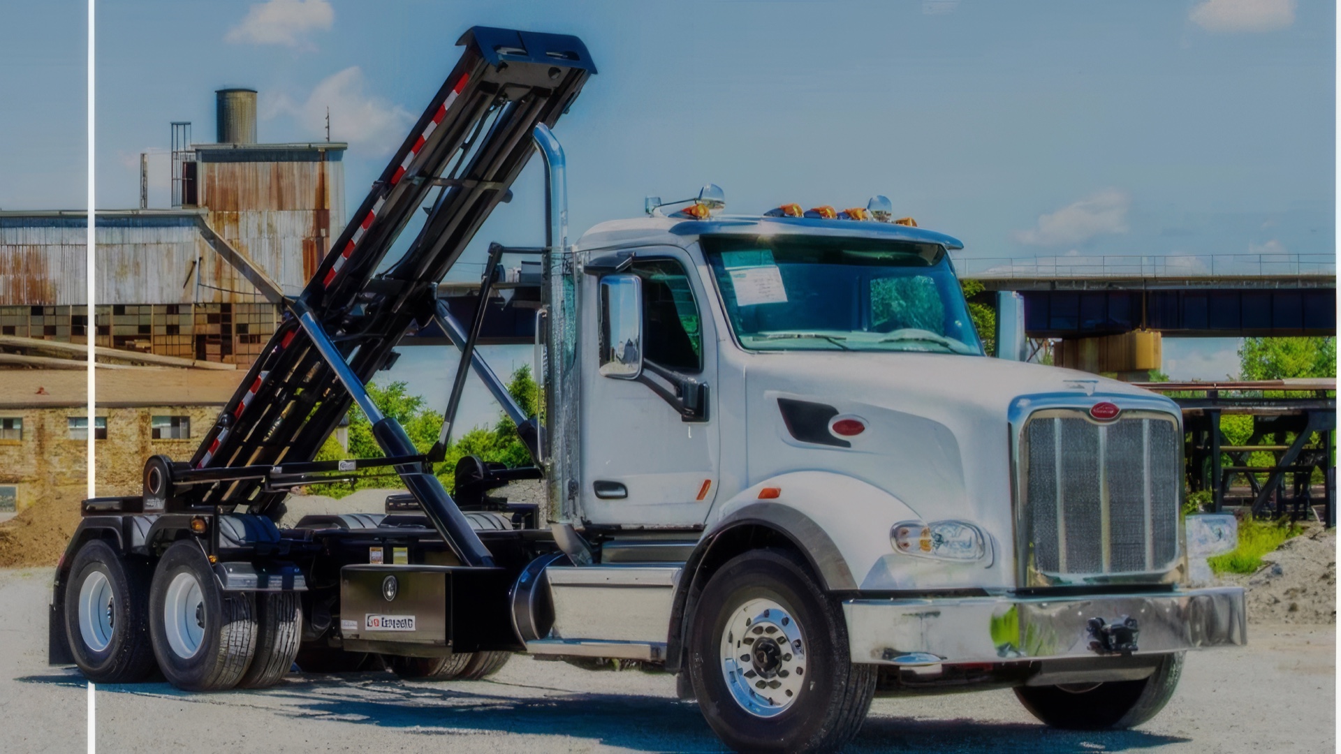 White Peterbilt roll-off truck with hoist raised at an industrial site